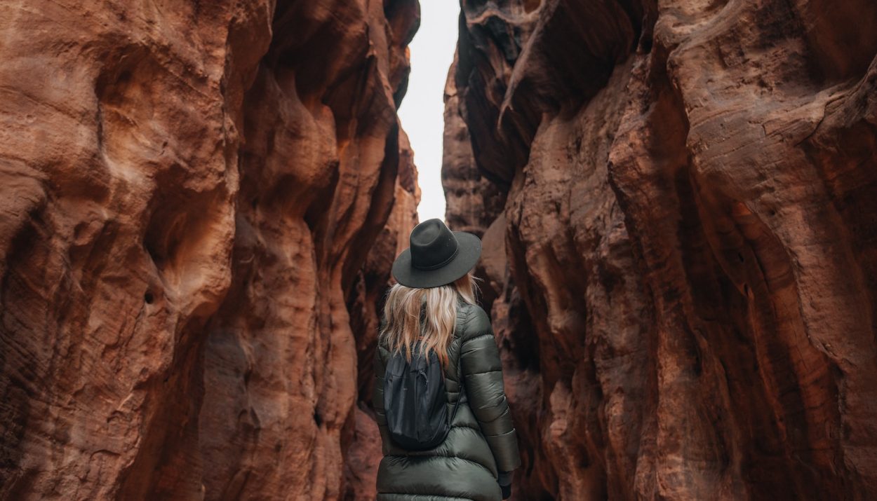 a woman in a hat and coat walking through a canyon